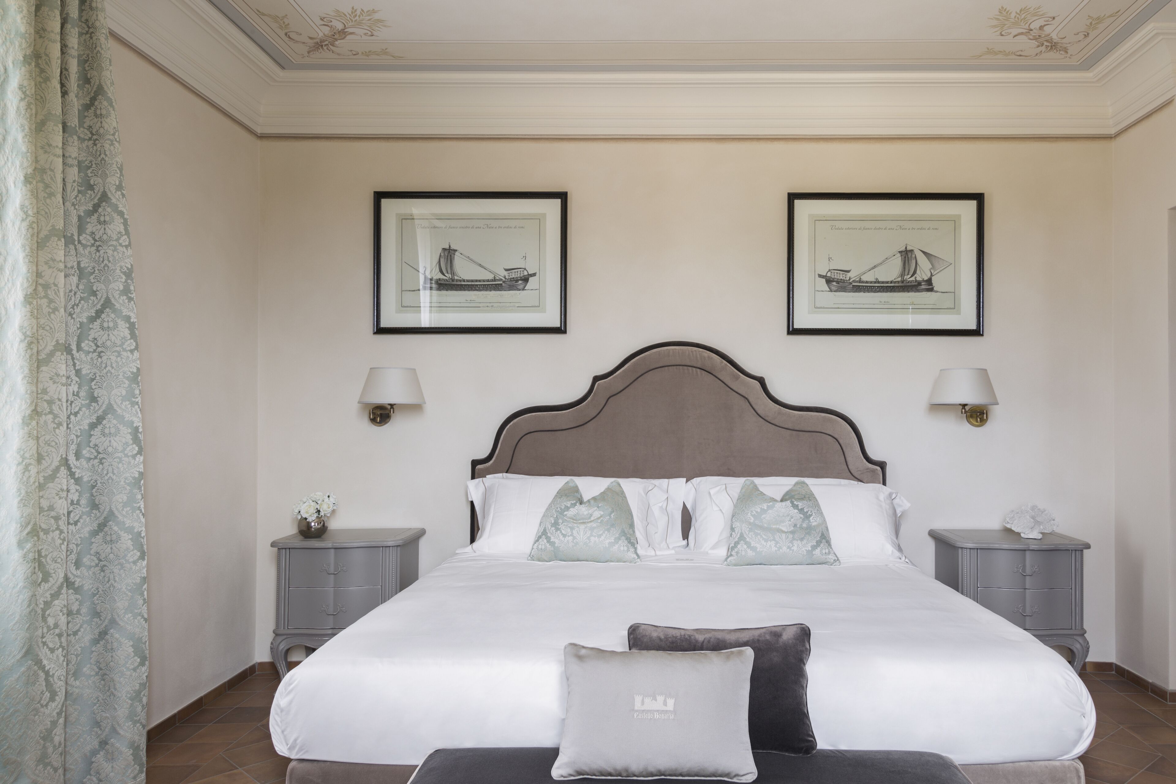 Une chambre bien rangée, avec un grand lit, deux tables de chevet et des œuvres d’art encadrées accrochées aux murs.