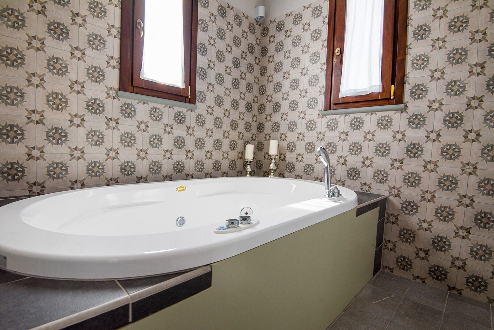 Un baño con una bañera independiente, dos ventanas y paredes con azulejos estampados.