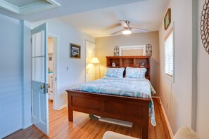 Une chambre à coucher avec un lit en bois, un ventilateur de plafond, une table de chevet, une lampe et une fenêtre avec des stores.