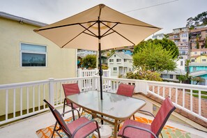 Une table en verre, quatre chaises et un parasol beige sur un balcon doté d’une balustrade blanche.