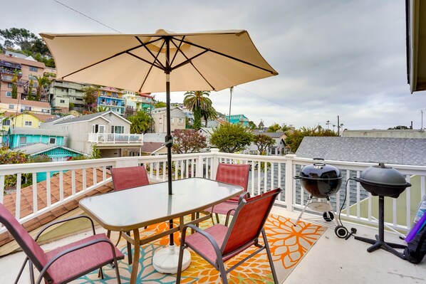 Un balcon avec une table et des chaises, un barbecue et une vue sur des bâtiments aux couleurs vives.