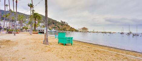 A beach with a turquoise chair, palm trees, and a calm sea with boats.