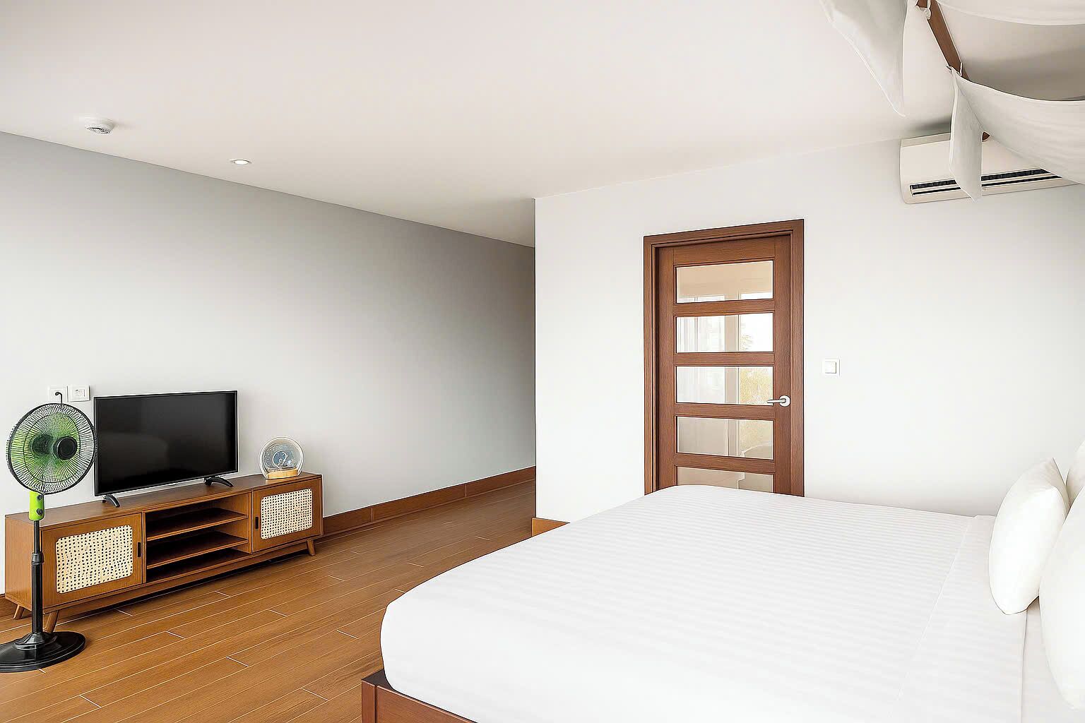 A bedroom with a bed, a TV, a fan, and a wooden cabinet.