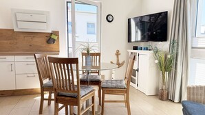 Een moderne woonkamer met een glazen eettafel, houten stoelen, een televisie en uitzicht op buiten.