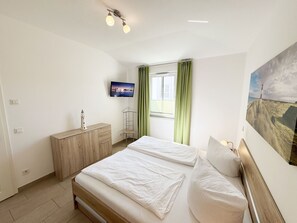 A bedroom with two beds, a TV, a desk, and a window with curtains.