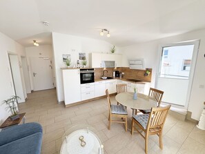 A modern kitchen with white cabinetry, a built-in oven, and a dining area with a round table and chairs.