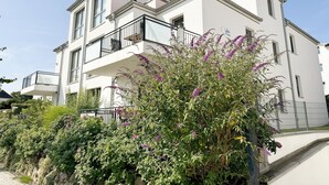 Een modern, twee verdiepingen tellend gebouw met balkons en een tuin vol paarse bloemen.
