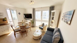Een goed verlichte woonkamer met een bank, eettafel, stoelen, een televisie en een boekenkast.