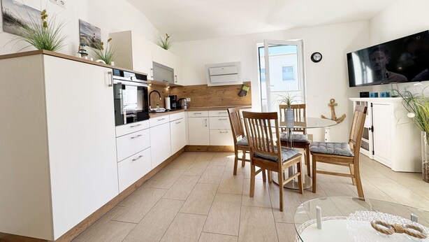Een moderne keuken met witte kasten, een houten aanrecht en een eethoek met houten stoelen en een glazen tafel.