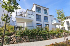 Un immeuble résidentiel moderne à plusieurs étages, doté de balcons, d’un mur de soutènement en pierre et d’un chemin piétonnier pavé.