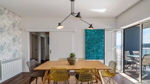 Uma área de jantar com mesa de madeira, cadeiras amarelas, planta em vaso e uma parede de destaque em tons de verde-água.