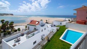 Hotel moderno com piscina no terraço, vista para a praia e uma pequena área de jardim.