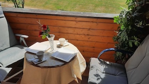 Een kleine buitentafel met een bloemenvaas, een kopje en een tablet op een houten terras.