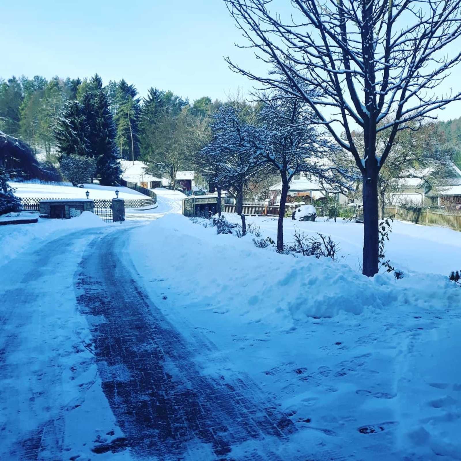 A snow-covered road with houses and trees in the background.