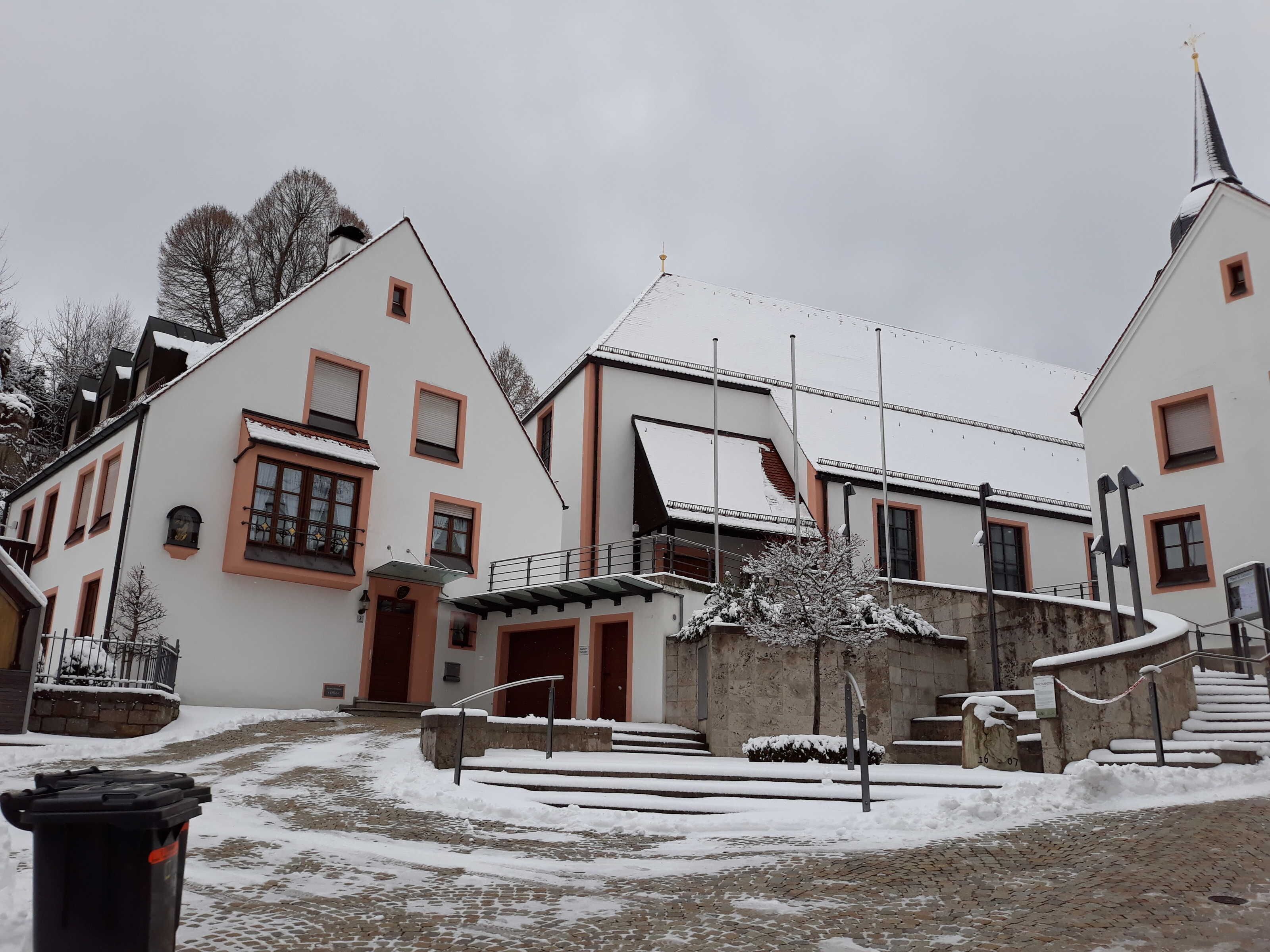 A building with a snow-covered roof, a stone staircase, and a paved courtyard.