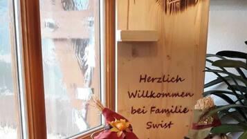 A wooden sign with a heart-shaped cutout and text welcoming guests to a family home.
