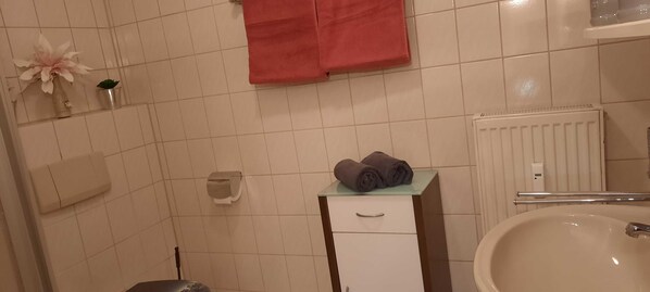 Un baño con lavamanos blanco, toallero con una toalla doblada, inodoro y radiador.