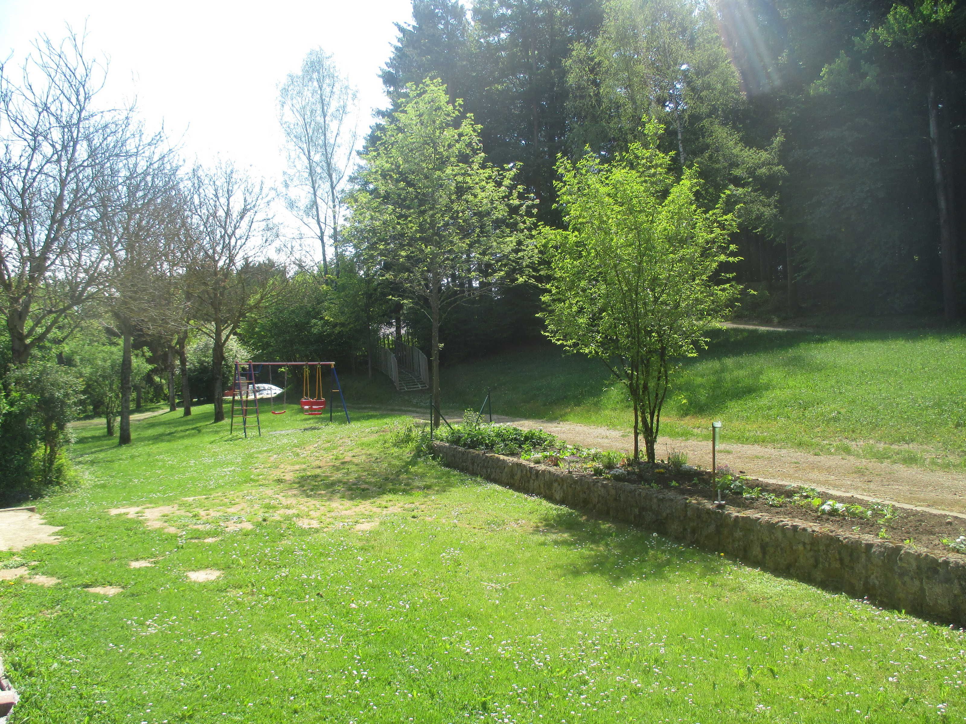 A grassy park with a swing set, a stone wall, and trees.