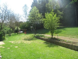 Ein Park mit Rasenfläche, einer Schaukel, einer Steinmauer und Bäumen.