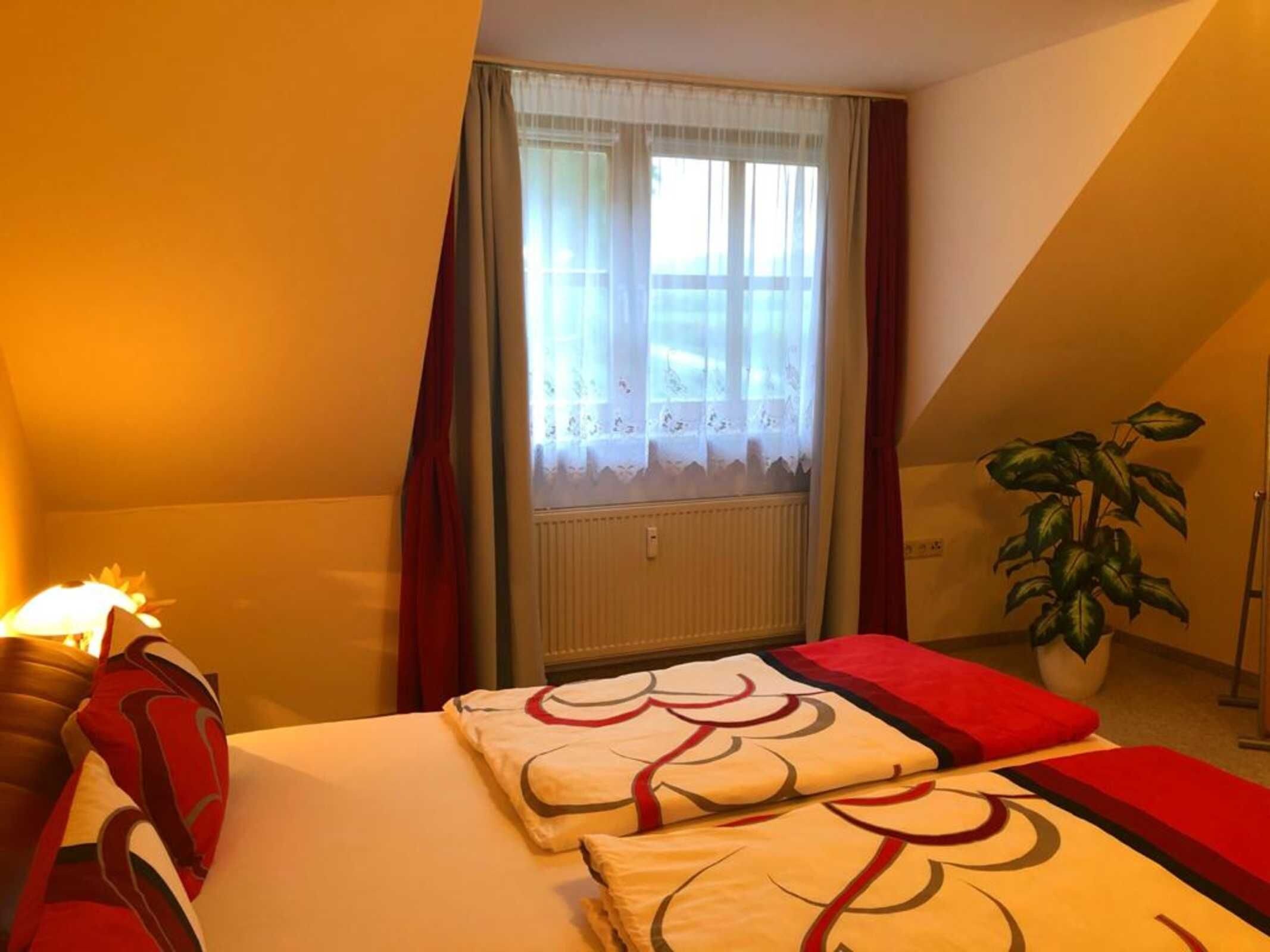 Un dormitorio con cama, ventana con cortinas, radiador y planta en maceta.