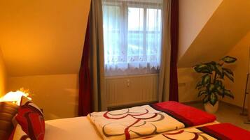 Una camera da letto con un letto, una finestra con tende, un termosifone e una pianta in vaso.