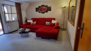 Ein Wohnzimmer mit einem roten Sofa, einem kleinen Tisch und einer Stehlampe.