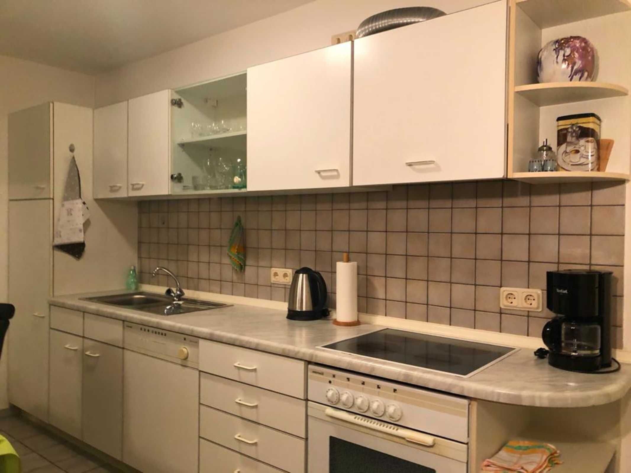 Eine Küche mit weißen Schränken, einer Spüle, einem Herd und einer Kaffeemaschine.