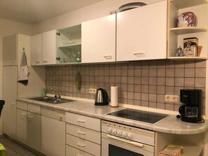 Une cuisine avec des meubles blancs, un évier, une cuisinière et une machine à café.
