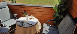 A small outdoor table with a vase of flowers, a cup, and a tablet on a wooden deck.