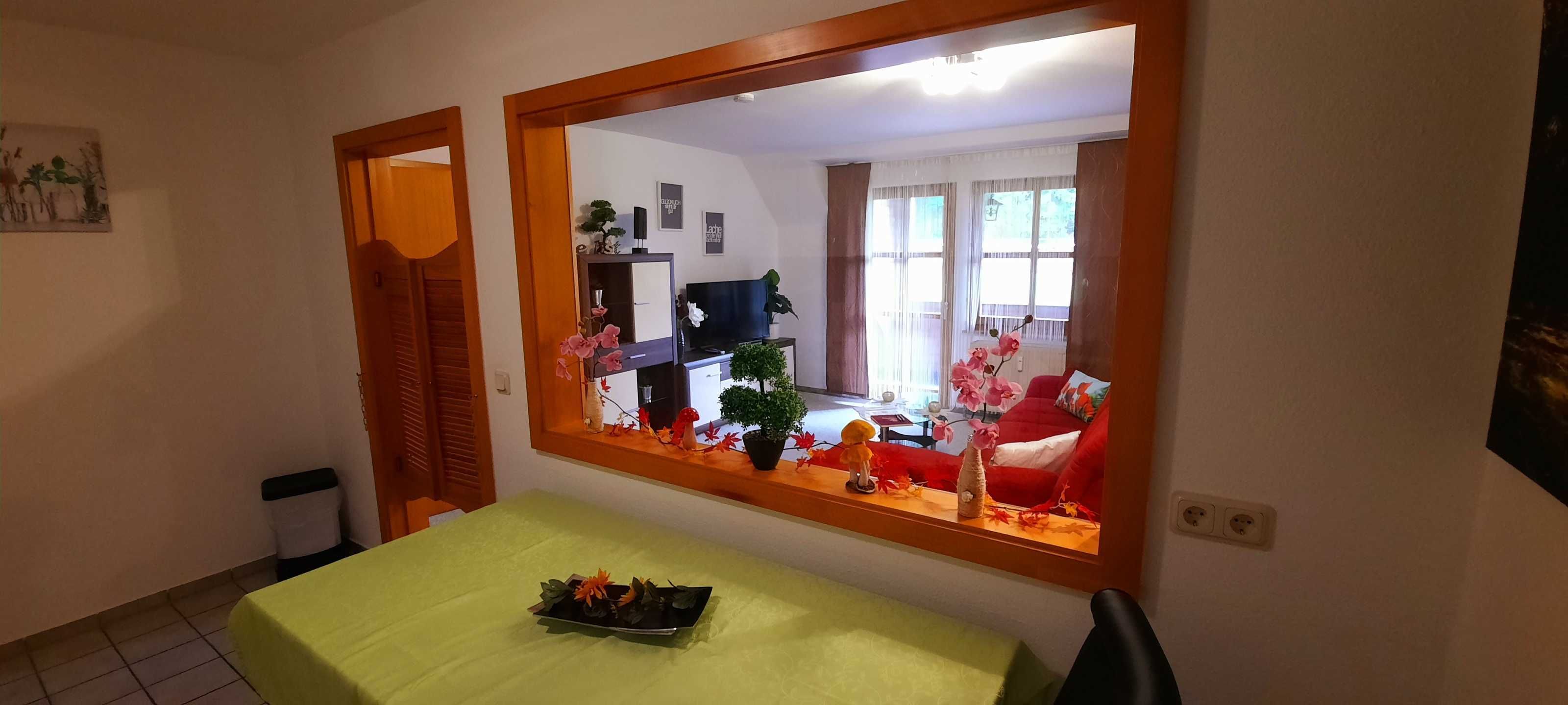 A dining area with a table, chairs, a mirror, and a view of a living room with a sofa and a TV.