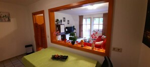 Un coin repas comprenant une table, des chaises, un miroir et donnant sur un salon avec un canapé et un téléviseur.