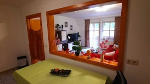 Een eetgedeelte met een tafel, stoelen, een spiegel en uitzicht op een woonkamer met een bank en een televisie.