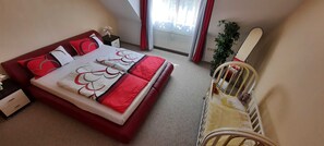 Une chambre à coucher avec un lit, une table de chevet, une commode, une fenêtre avec des rideaux et un berceau.