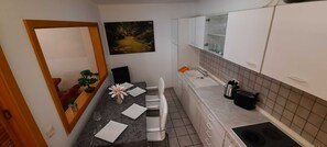 Une cuisine de taille réduite comprenant un coin repas, un évier, des placards et un tableau accroché au mur.