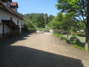 Ein gepflasterter Innenhof mit einem Gebäude links, einem kleinen Tor und Bäumen rechts.