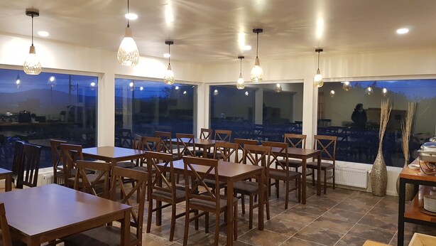 Un restaurante con mesas y sillas de madera, ventanas amplias y lámparas colgantes.