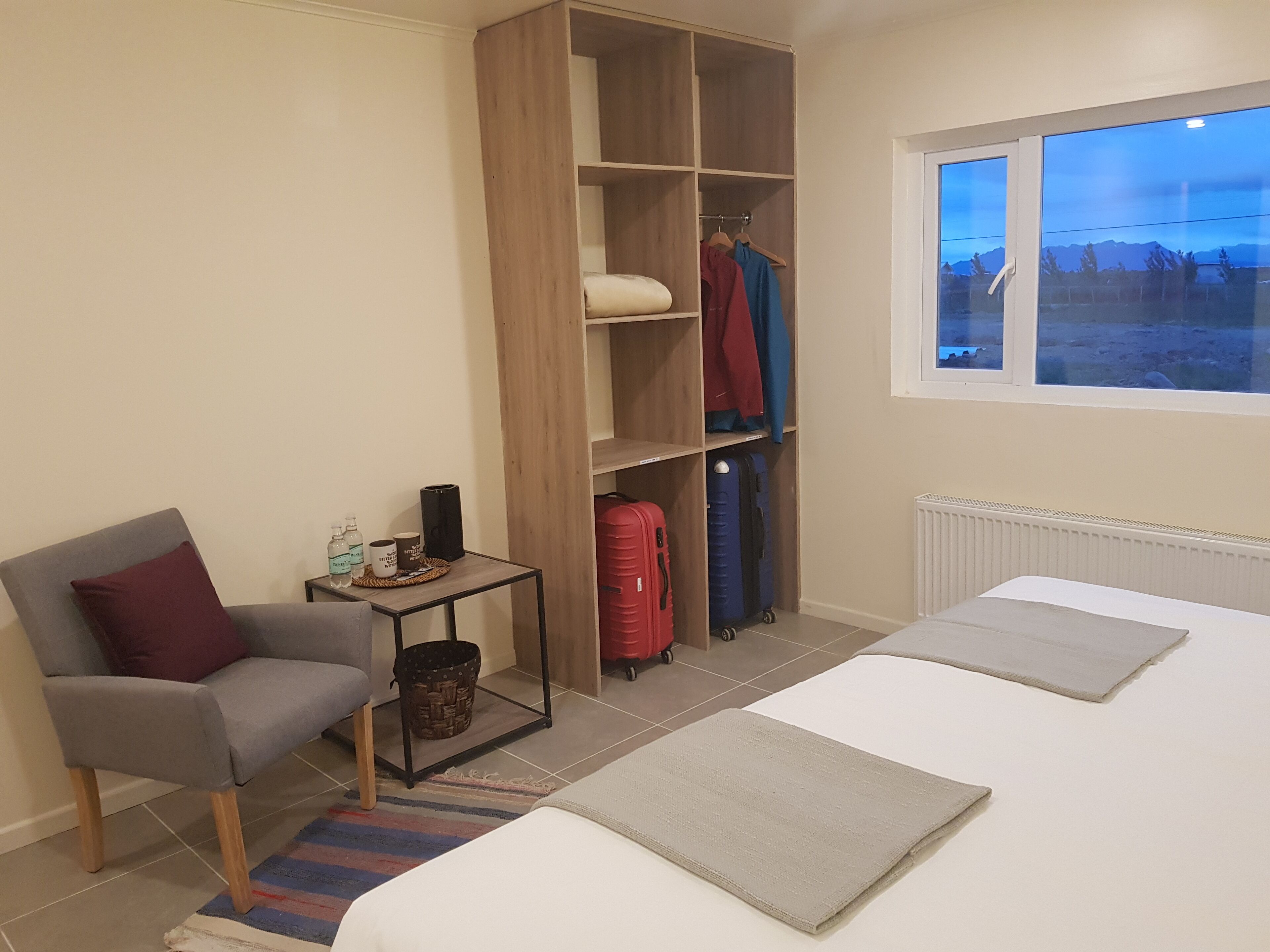 Um quarto com cama, poltrona, guarda-roupa e janela com vista.