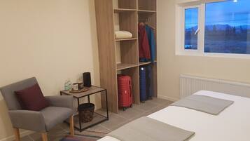 Um quarto com cama, poltrona, guarda-roupa e janela com vista.