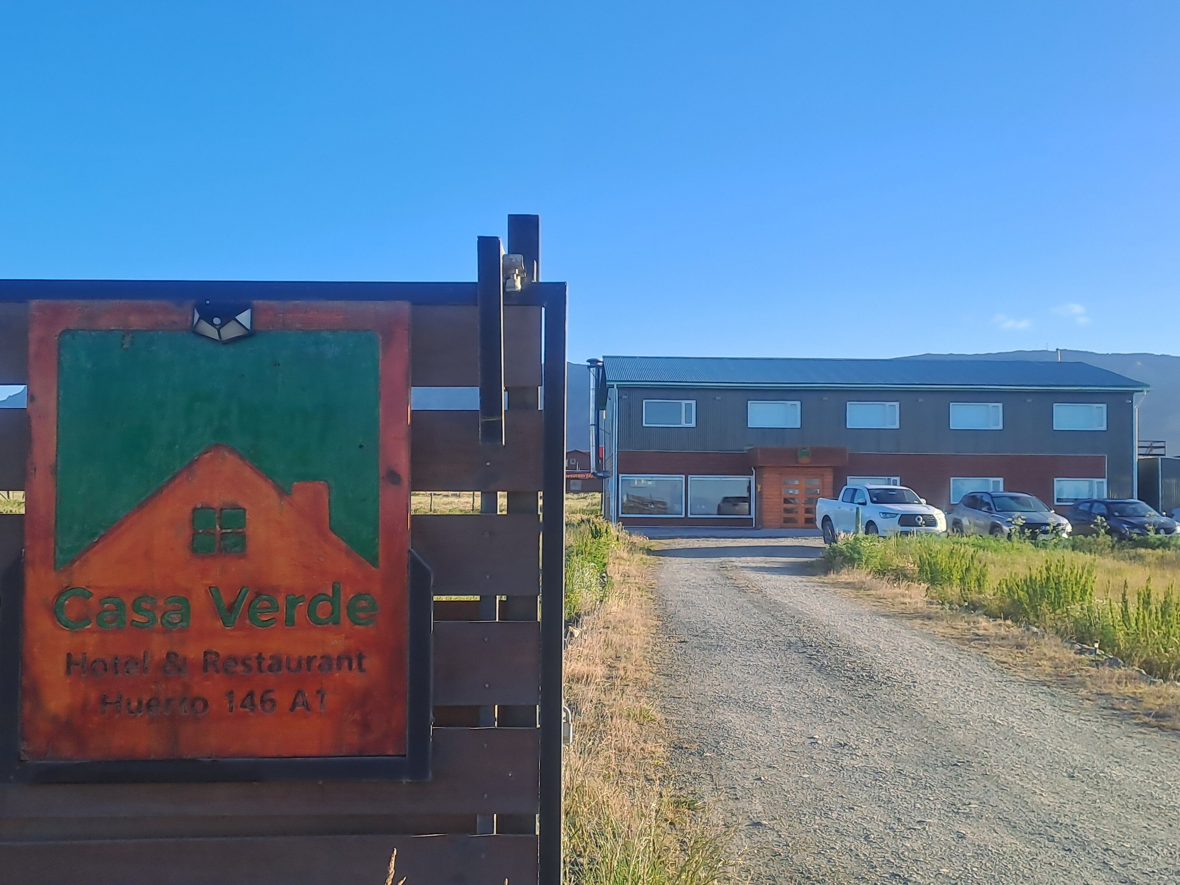 A sign for Casa Verde Hotel & Restaurant with a view of a modern building and parked cars in the background.