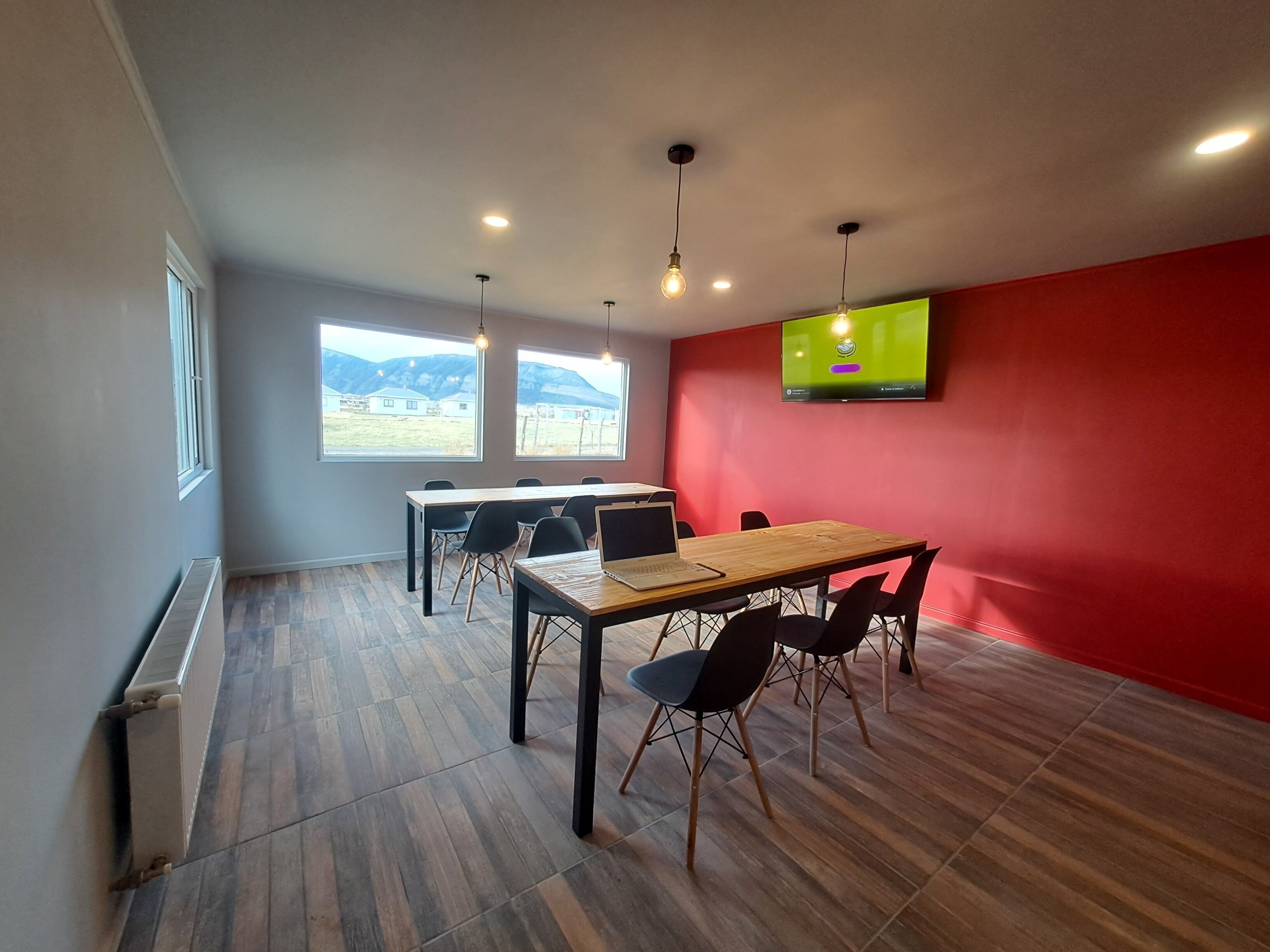 A modern meeting room with a wooden table, black chairs, a laptop, and a TV on the wall.