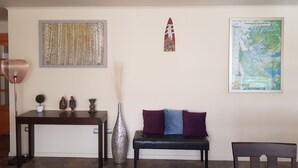 Un salón con una mesa de centro de madera oscura, un sofá con cojines morados, un jarrón alto y un mapa enmarcado en la pared.