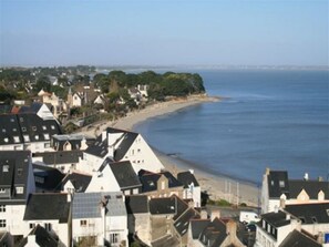 Un pueblo costero con casas a lo largo de la playa, una vista despejada del mar y el perfil distante de una ciudad.