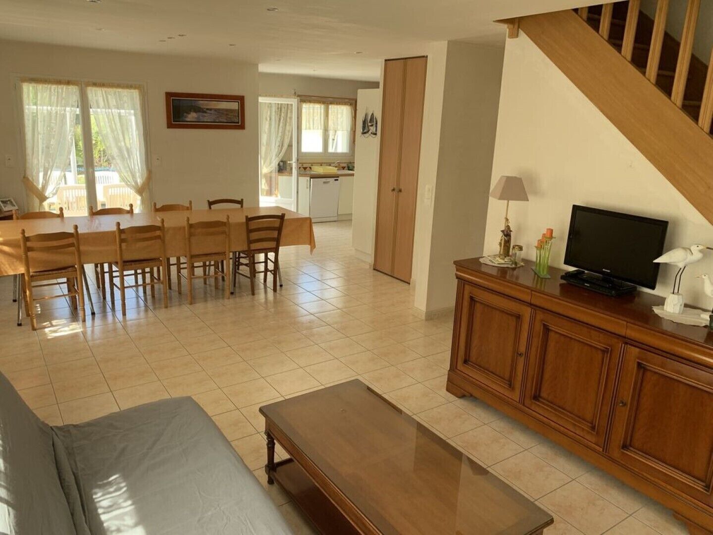 Un vaste espace de vie comprenant une table et des chaises en bois, un canapé, un téléviseur posé sur un meuble en bois et un escalier.