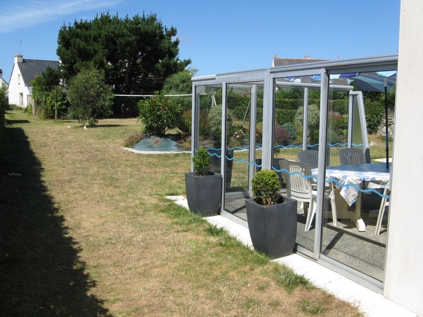 A covered patio area with a table and chairs, surrounded by potted plants and a view of a garden.