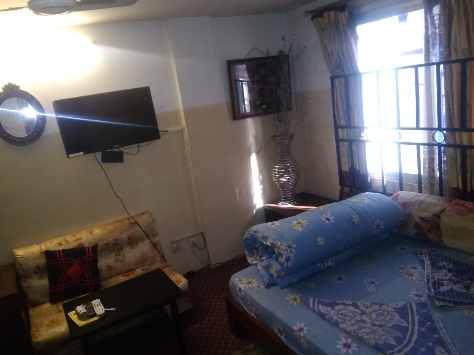 A living room with a sofa, a television mounted on the wall, a vase on a side table, and a window with curtains.