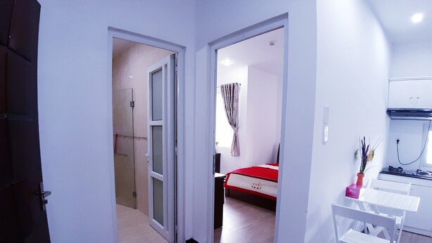 A hotel room with a bed, a small kitchen area, and a bathroom visible through an open door. - SERVICED APARTMENT FOR RENT IN PHU NHUAN DISTRICT (Ho Chi Minh)