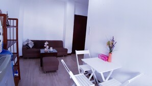A compact living space with a sofa, a small table with chairs, a potted plant, and a kitchenette area. - SERVICED APARTMENT FOR RENT IN PHU NHUAN DISTRICT (Ho Chi Minh)