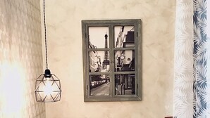 En væg med en geometrisk lampe og et indrammet vindue der afspejler et gadesceneri.
