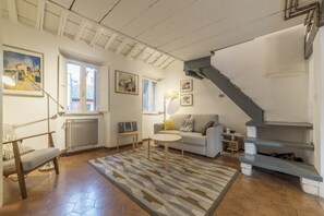 A living room with a sofa, a coffee table, a lamp, a radiator, and a staircase. - Modern and comfortable loft equipped with every comfort. Ideal for hosting 2 people, in approximately 55 m2 of space, it is located on the third floor of an elegant period building without a lift.It is located a few minutes walk from Piazza Navona, Panth (Roma)