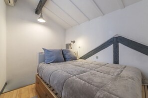 A bedroom with a bed, a wooden dresser, a desk, and a lamp.